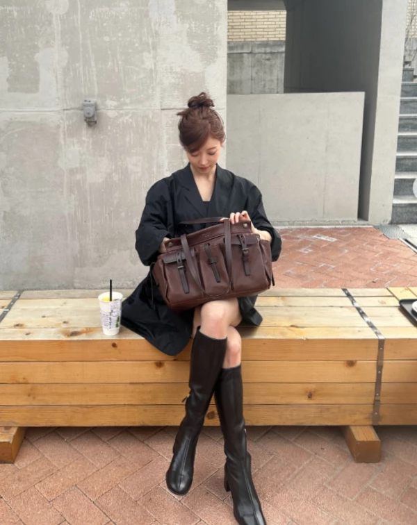 李世榮完全就是把「甜酷風」玩到極致的範本。上半身是一件設計感十足的蓬鬆黑色西裝外套,大大的領口露出鎖骨,看起來有點小女人的優柔,頭髮還綁了個超可愛的丸子頭,單看上半身,這絕對是走甜美路線的。但下半身,她反而大膽地配上了一雙過膝的黑色皮筒靴,露出那一段恰到好處的膝上處。這雙靴子的挺闊感跟上半身的蓬鬆感形成強烈對比,瞬間把甜美度轉化成一種甜美的的率性。