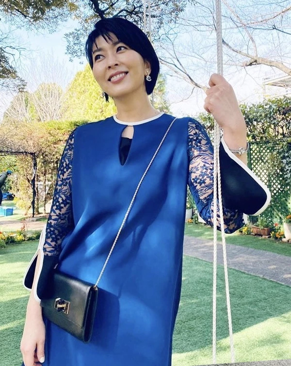 深藍色連身裙，在袖口處大面積拼接了細緻的藍色蕾絲花卉，並在領口做了小鏤空設計。微喇叭袖與白色滾邊的撞色細節，帶有濃濃的法式復古風情。穿著蕾絲時，熟齡女性最怕的就是顯得老氣或過於暴露，但我們不妨可以學學松隆子這樣，選擇具有與身上服裝的「同色系」蕾絲，讓肌膚隱約透出，既優雅又安全。最後再適度地搭配一款纖細的鏈帶小包，或閃耀的鑽石耳環、手鍊…等小珠寶點綴，貴氣又不顯老。