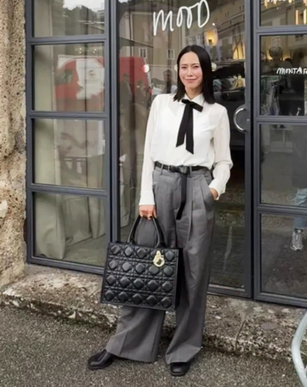 想穿出「知識份子」的高級感,搭法就在細節中。略帶透膚感的絲質襯衫,本身就很溫柔,但加上一條繫上的黑色緞帶領結,立刻多了點中性的帥氣。下半身,則是搭配高腰灰色打摺褲與皮帶,將腰線拉高、營造乾淨俐落的優雅氣質。一般人若想要把這條褲子穿好。如果身材不是那麼瘦,皮帶可以選細一點的,且褲管記得捲起來露出一點腳踝。就能「無痛拷貝」到日常辦公室。