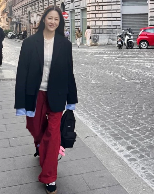 高賢廷在歐洲街頭漫步的街頭穿搭，大膽選用沉穩的黑色西裝外套，搭配米白色上衣與清涼感十足的藍條紋襯衫，最精彩的莫過於刻意露出的襯衫袖口與下襬，靠著這種「長、短不一」的層次細節，瞬間化解了西裝外套的正式感，增添視覺律動。下半身，則大膽搭配一條高飽和度的紅色寬褲，這抹重色豔彩，不僅點亮了街頭氛圍，更與黑色外套混搭出一種對比的活力。 對於想學習的同齡大眾來說，我們只要敢於在黑、白、灰的基本單品中，加入一抹鮮明色彩，就能瞬間打破僵硬線條，在專業感中保留住如藝術家般的年輕氣場。