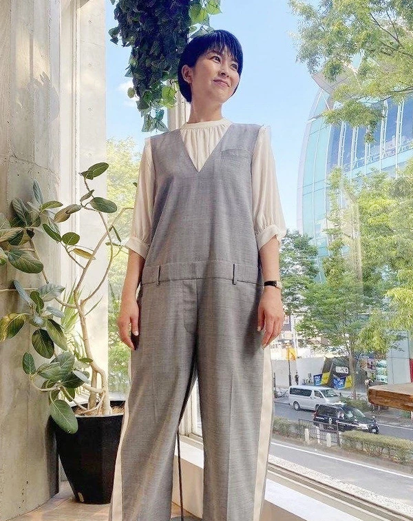 松隆子身穿一件深V剪裁的細緻灰色連身褲，內搭米白色微澎袖的雪紡襯衫。連身褲的兩側，帶有白色織帶的拼接細節，腰間則有類似西裝褲頭的設計，直接將工裝的率性與正裝的俐落完美結合。