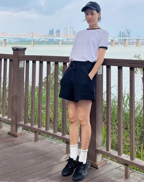 金瑞亨穿著簡單的白T恤，搭配黑色高腰運動短褲，最絕妙的細節在於她腳上的黑色運動鞋與那雙拉得高高的「純白長襪」，長襪的加入立刻注入了美式復古運動員的活力，完全消除了大齡女子穿短褲可能帶來的居家感。想要運動風不顯邋遢，細節配件（帽子與襪子）絕對是關鍵！不僅能修飾腿型，還能增添日、韓流行的街頭少女感。