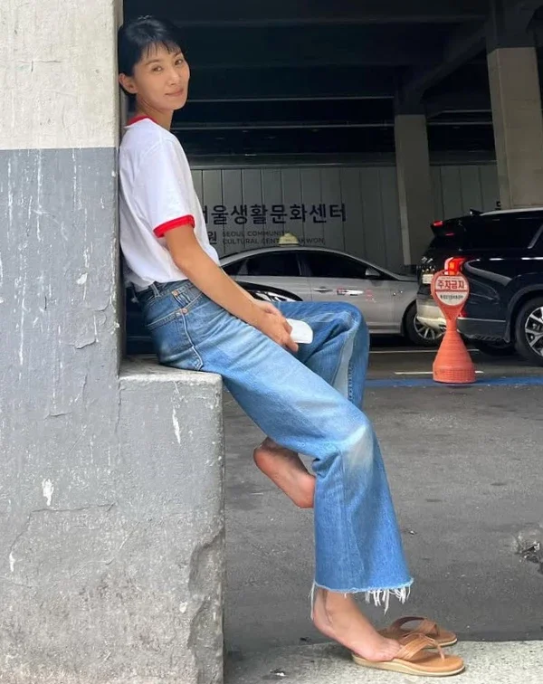 想要呈現鄰家姐姐的無壓迫感，這套請直接拷貝！一件簡單的滾邊白T，搭配一條刷色自然的九分微喇叭牛仔褲，褲腳的抽絲細節多了一絲不羈。她甚至連鞋子都選了最放鬆的皮革夾腳涼鞋。這種極致慵懶的穿搭，反而襯托出她清爽的短髮與乾淨的面容。減齡不需要層層堆疊，有時簡單點搭配，反而能讓人看起來年輕10歲。