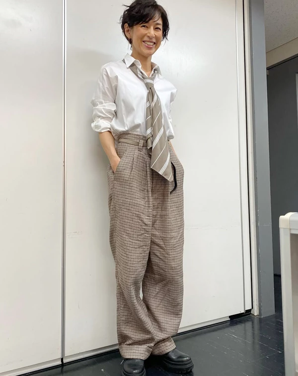 鈴木保奈美將看似乖巧的白襯衫與高腰千鳥格紋寬褲組合，卻高明地解開領口、將袖子隨意捲起，並配上一條大地色系的寬領帶。一般人穿白襯衫與格紋褲最怕像制服或顯老，我們可以學她故意不把領帶打得太嚴謹，讓它像圍巾般鬆散地掛在頸間，再踩上一雙硬挺的黑色厚底樂福鞋或短靴，就能瞬間拉滿英倫學院風的帥氣，巧妙達到減齡效果。