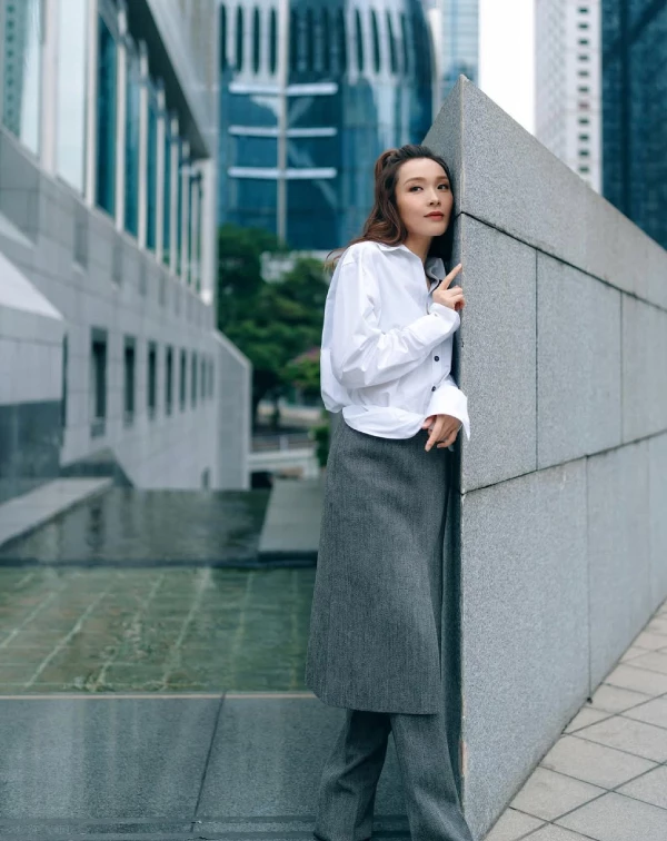 李佳芯完美演繹了什麼叫作走在時尚前端的「高智感逆齡」。我們平常穿白襯衫配西裝褲總覺得太嚴肅,快學她這招進階步驟!先穿上一件俐落的寬版剪裁白襯衫,下半身大膽嘗試「裙褲疊穿」—在灰色西裝寬褲外面,再疊加一條同色系的一片裙。這個技巧,能瞬間打破中規中矩的沉悶感。教學關鍵在於紮起一個高挺、帶有捲度的馬尾,把視覺重心向上拉,整個人不僅顯得高挑有精神,更散發出一股不用討好任何人的高級時髦感。
