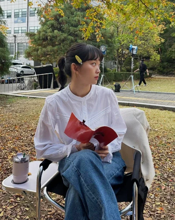 白襯衫加牛仔褲人人會穿,但秦基周聰明地挑選了帶有微宮廷風壓褶與小立領設計的白襯衫,少了上班族的嚴肅,多了幾分浪漫,瞬間把視覺年齡拉回20出頭。一般人日常在穿搭白襯衫時,可以捨棄過於合身、硬挺的正式版型,改選材質柔軟、帶有微落肩或精緻細節的款式。再配上一款亮色系的髮飾,就能輕鬆複製這種不費力的初戀感。