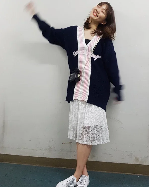 這套穿搭,則是展現了基周歐尼甜美的一面。她穿著深藍色V領開襟衫,開襟處有可愛的粉色條紋和字母設計。下半身,則是搭配白色蕾絲長裙及厚底白鞋。這種混搭,既有開襟衫的復古甜美,又有蕾絲裙的仙氣,最後用運動鞋收尾,讓整體造型不會過於嬌柔造作。