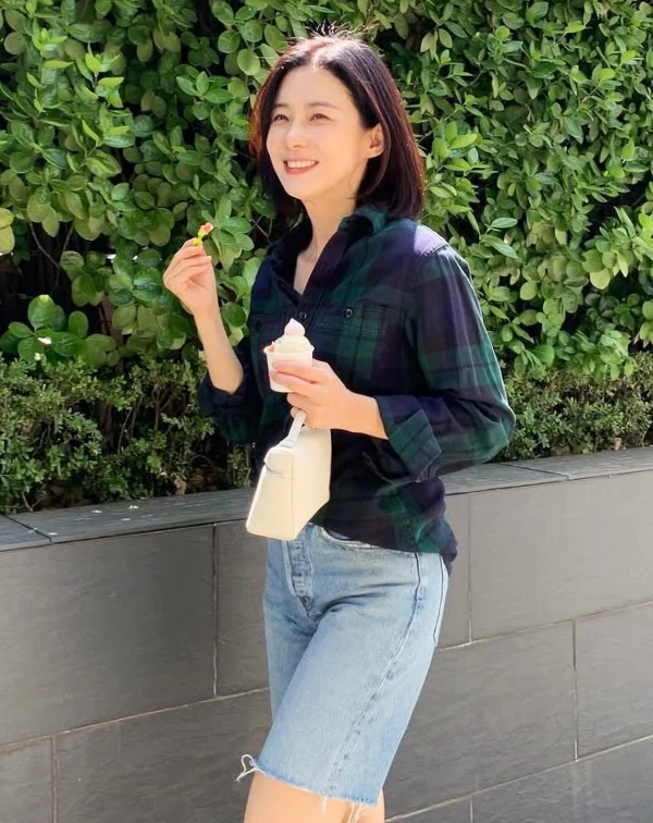 天啊，這套說是大學生剛下課我都信！李寶英用最經典的綠色深色格紋襯衫，隨意捲起袖口，再搭配一條帶有洗舊抽絲感的高腰牛仔五分褲。襯衫下擺只塞前面，不僅能抓出腰身比例，更散發出一股大方不造作的陽光率性。手上那咖純白化妝包造型手提包更是神來之筆，在滿滿的休閒感中點綴出精緻度，吃個冰也時髦得不像話！