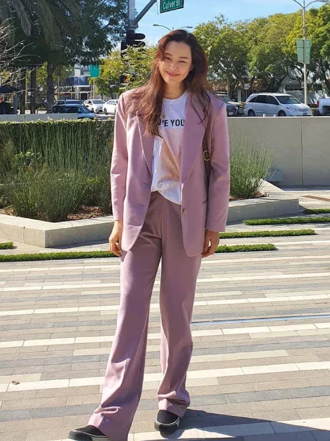 這套煙粉紫色的西裝套裝真的太懂熟齡女性的心思了!李荷妮聰明地避開了過於嬌嗔的正粉色,選擇帶點莫蘭迪灰調的低飽和煙粉紫,既保留了夢幻浪漫的少女感,又兼具成熟女人的優雅氣場。內搭一件簡單的印花白T,腳踩休閒平底鞋,將正式感的正裝穿得如此輕鬆自如,展現出令人羨慕的甜美鬆弛感。