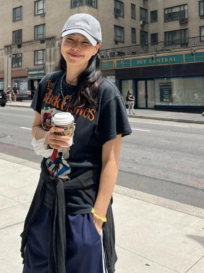李荷妮以黑色復古搖滾T恤、腰間繫上薄外套,再戴上一頂灰色棒球帽,隨性捧著咖啡的模樣簡直帥翻!這種帶有美式街頭感的混搭,完美演繹了時髦的最高境界。棒球帽與洗水復古T恤,是絕佳的減齡單品!如果覺得單穿T恤太單調,可以在腰間或肩上綁一件薄外套或格紋襯衫,增加視覺層次之外,還能順便遮擋臀部線條,實用又好看。