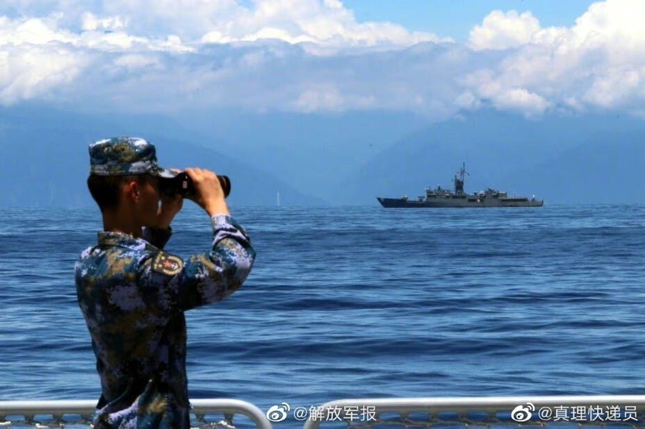 《解放軍報》微博公布的照片，顯示演訓中的解放軍用望遠鏡遙望台灣軍艦，背景的台海海岸清晰可見。（《解放軍報》微博圖片）
