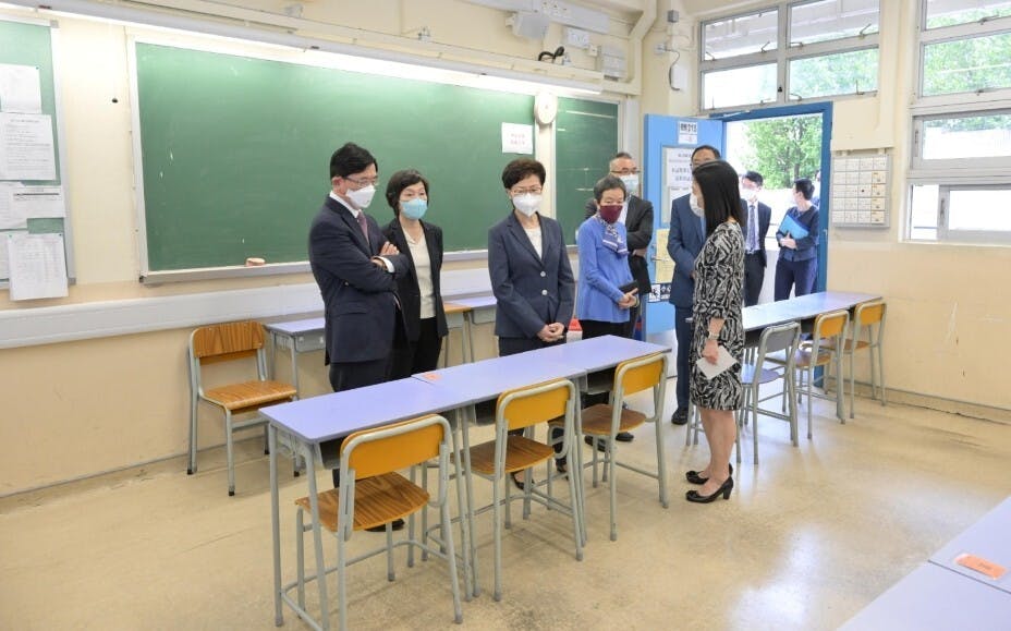 特首林鄭月娥（左三）在教育局副局長蔡若蓮（左二）及考評局主席容永祺（左）等陪同下，到訪中學文憑考試試場之一的金文泰中學，了解校方的防疫措施。圖為林鄭月娥聽取金文泰中學校長黎妙儀（前右）講解校方的防疫措施。（政府新聞處圖片）