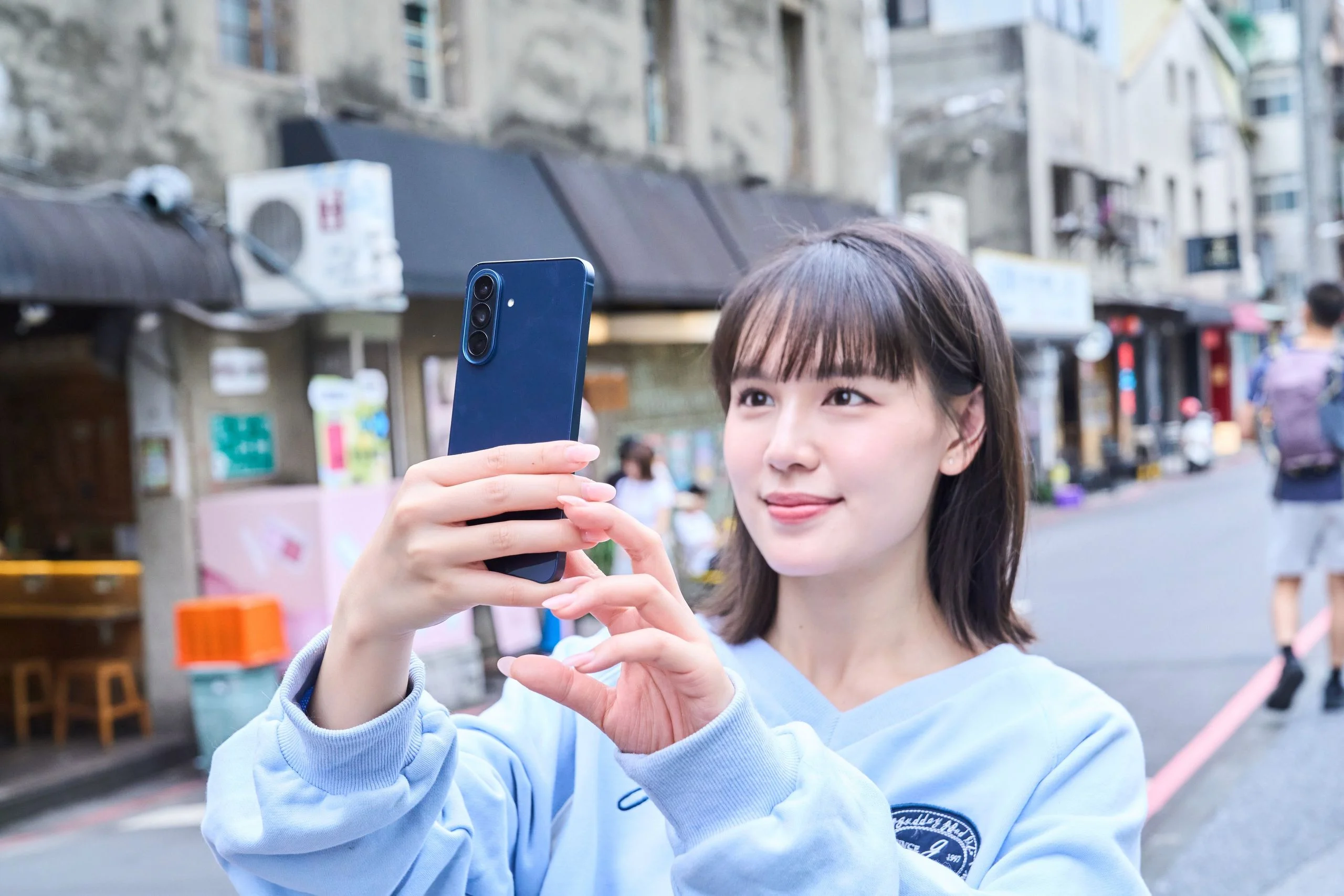 Model 拿著雅痞藍 Galaxy A57 5G 戶外自拍情境照