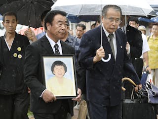 Mikio Watanabe, holding a portrait of his late wife Hamako, walks into the Fukushima District Court in Fukushimaima