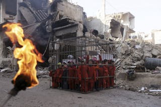An activist holds a burning torch near children carrying banners inside a cage during a protest against forces loyal to Syria's 