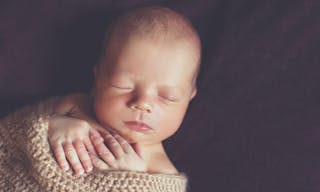 Portrait of a sleeping newborn baby wrapped in a knitted blanket beige handles hold near the chin,a little fluffy hair,portrait 