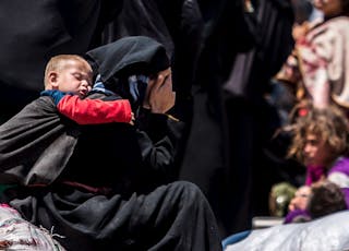 A woman reacts as she rests from walking back to Tel Abyad town