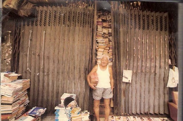 「何老大」在其上海街書店前留影，店內的書堆到天花頂像一座山。