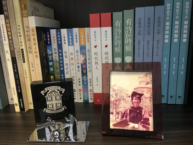 書架上區聞海的著作，以及1981的畢業照。攝於2018年。（受訪者提供圖片）