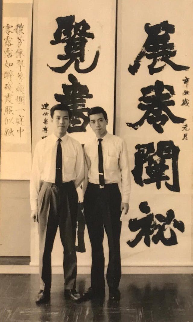 作者（左）與長兄靳埭強（右）攝於建公書專師生展，年份應是60年代，雖然區老師的巨型對聯上寫「辛丑」，但未必是展覽時的年份。（作者提供）