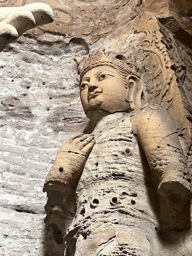 這尊立像身軀高挑,頭戴冠飾,一手抬於胸前做說法或施願姿勢,身上滿是風蝕孔洞與剝落痕跡,屬於早期的北魏佛像。