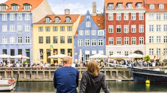 Tourists enjoying the scenic summer view of Nyhavn pier. Colorful building facades with boats and yachts in the Old Town of Copenhagen, Denmark